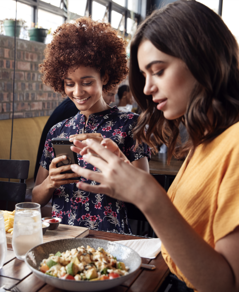 Two women taking pictures of their plates at a restaurant