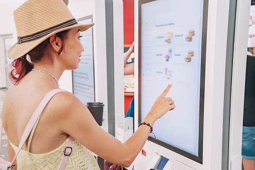 A customer uses a touchscreen terminal or self-service kiosk to order at a fast food restaurant