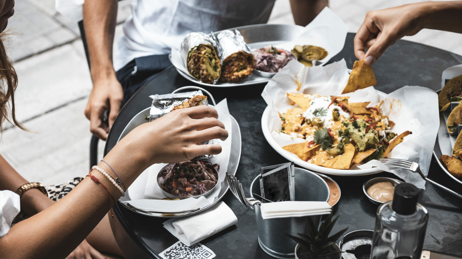 3 peoples sharing a plate of nachos